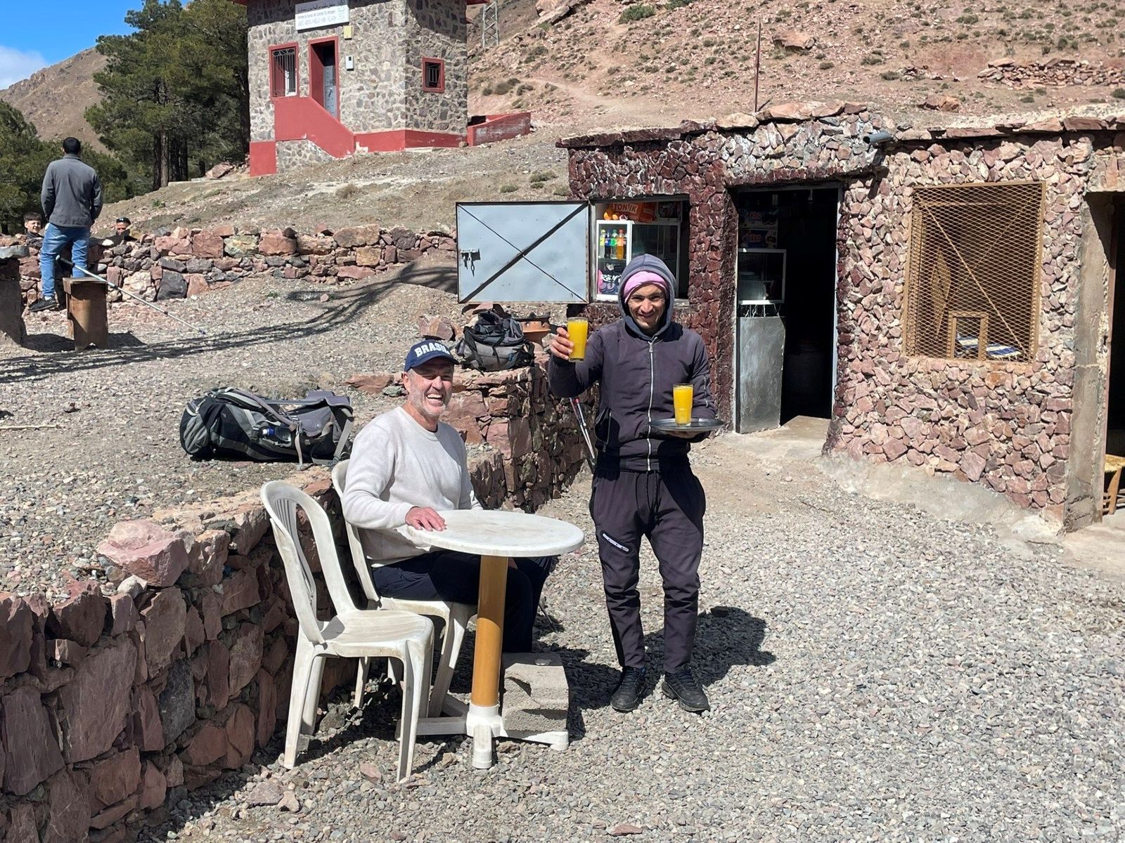 A traveler being served fresh orange juice outside a stone shop along High Atlas Mountains hiking trail