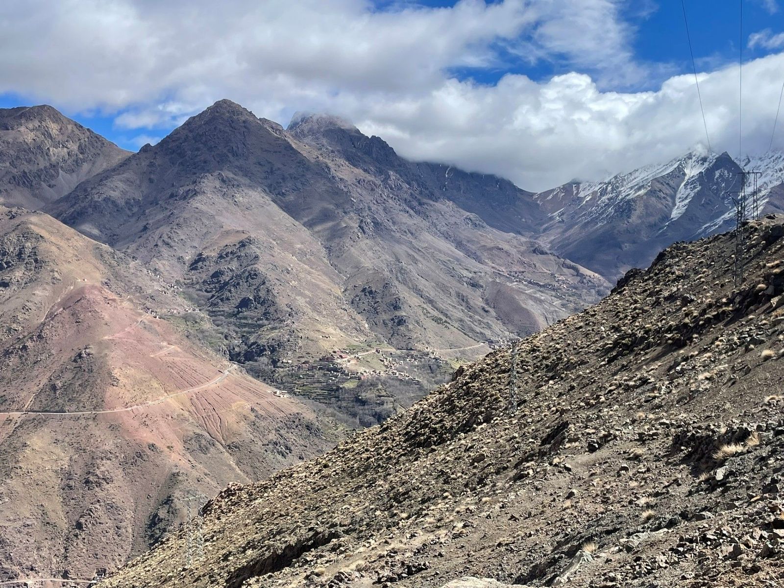 A winding mountain road and distant valleys in the cloud-capped ridges of the High Atlas Mountains in Morocco.