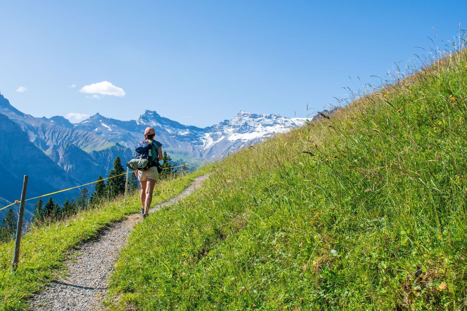 Hiker with a backpack walking along a narrow hiking in a hillside near Adelboden, Switzerland.