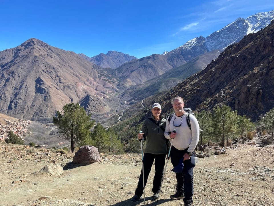 Hikers with trekking poles standing on a high trail that overlooks the High Atlas region of Morocco.